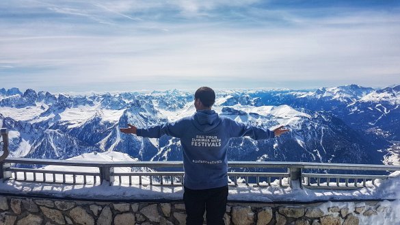 standing at the top of the Passo Pordoi with arms outstretched and the Dolomites in the background
