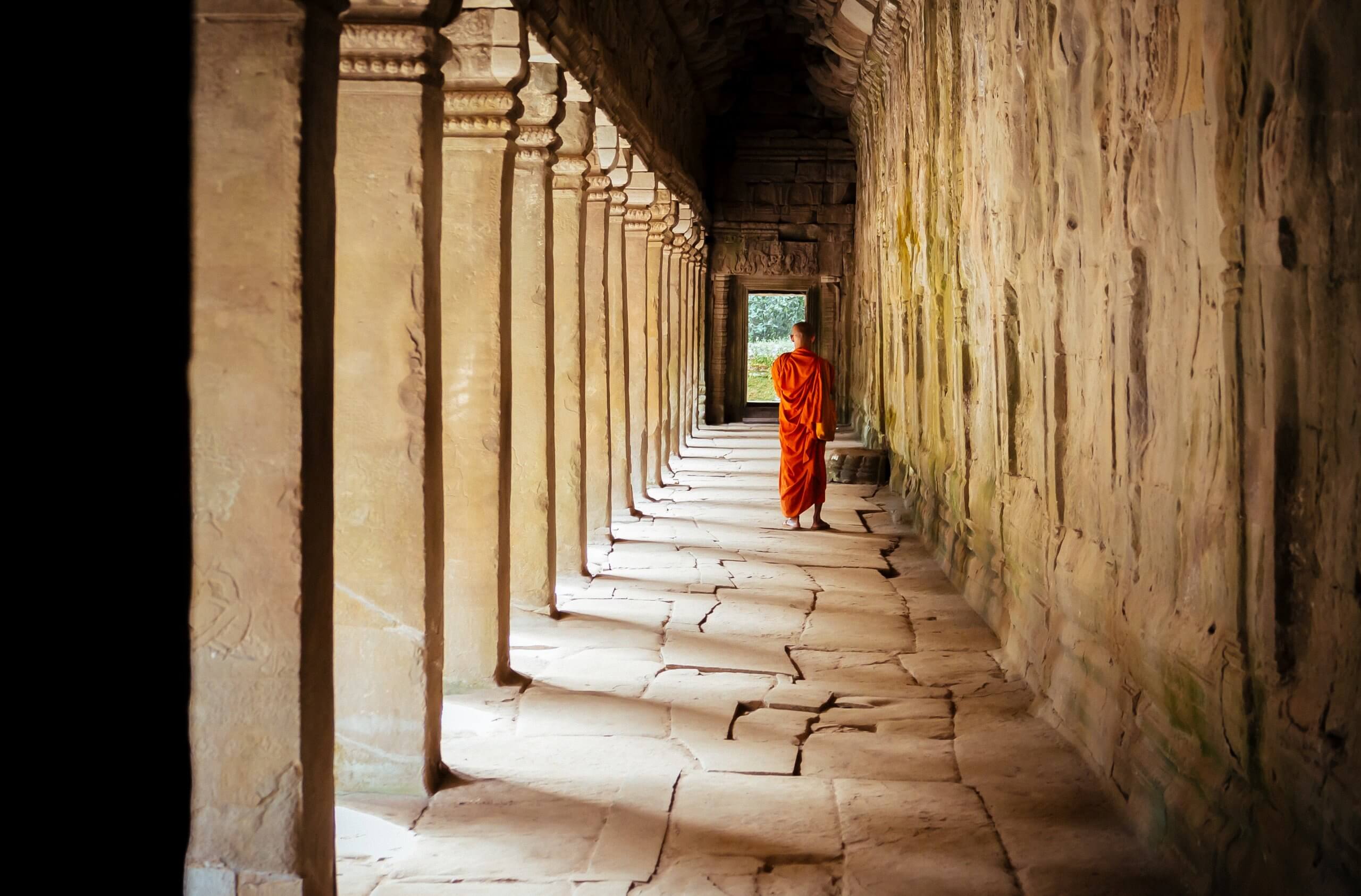 monk in orange robe far camera walking away in a cambodian temple corridor