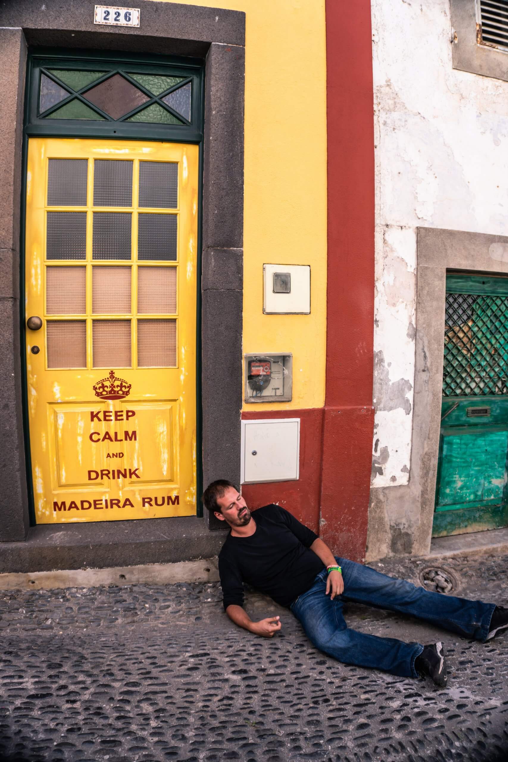 dave lying on the ground pretend drunk near a colourful yellow door saying keep calm and drink madeira rum