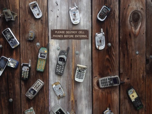 phones broken and nailed to a fence with the sign "please destroy cell phones before entering"