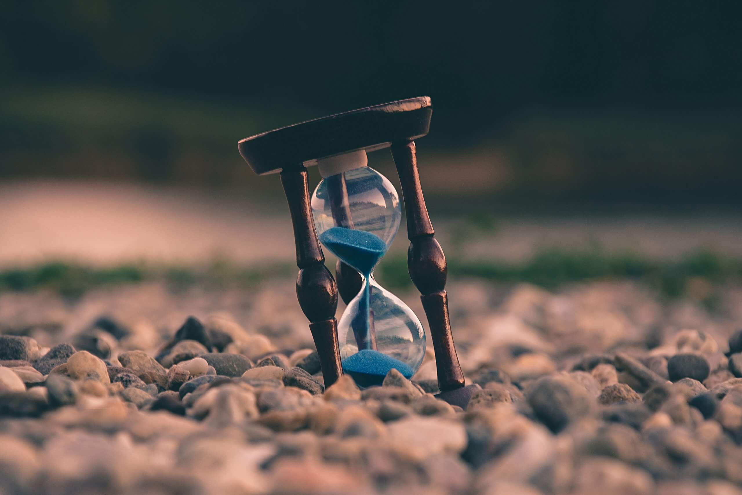 hourglass with blue sand tilted on a pebble beach