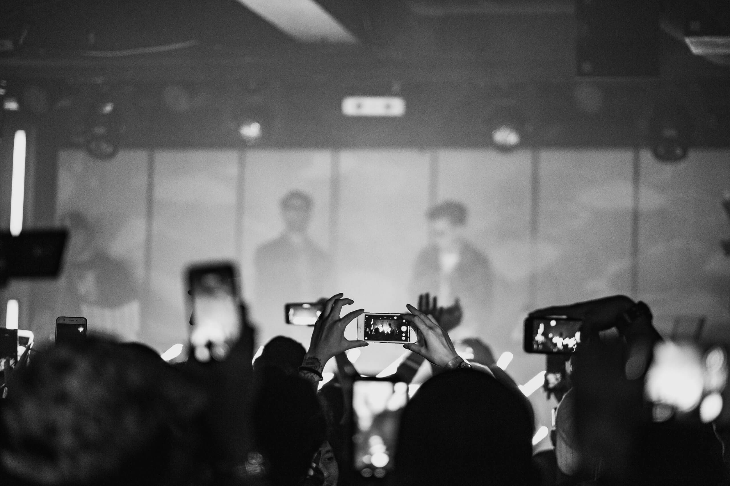 people at a concert all holding up phones and filming the event