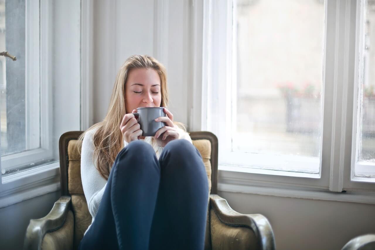 women relaxed and cosy in chair by window eyes closed and drinking a cuppa