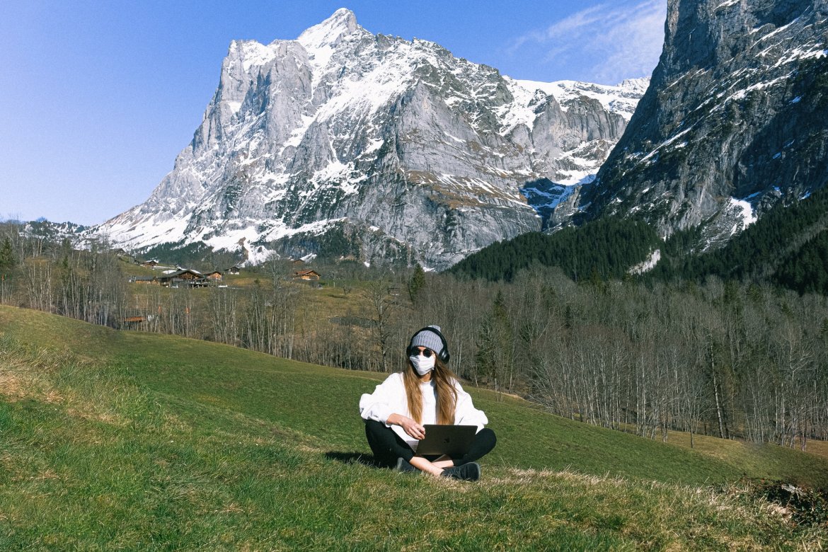 women wearing mask guarding against coronavirus in italy sitting on laptop alone surrounded by the mountains