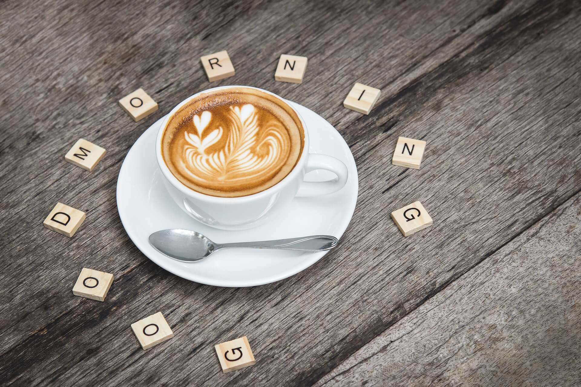coffee with coffee art and scrabble titles in a circular shape around showing good morning