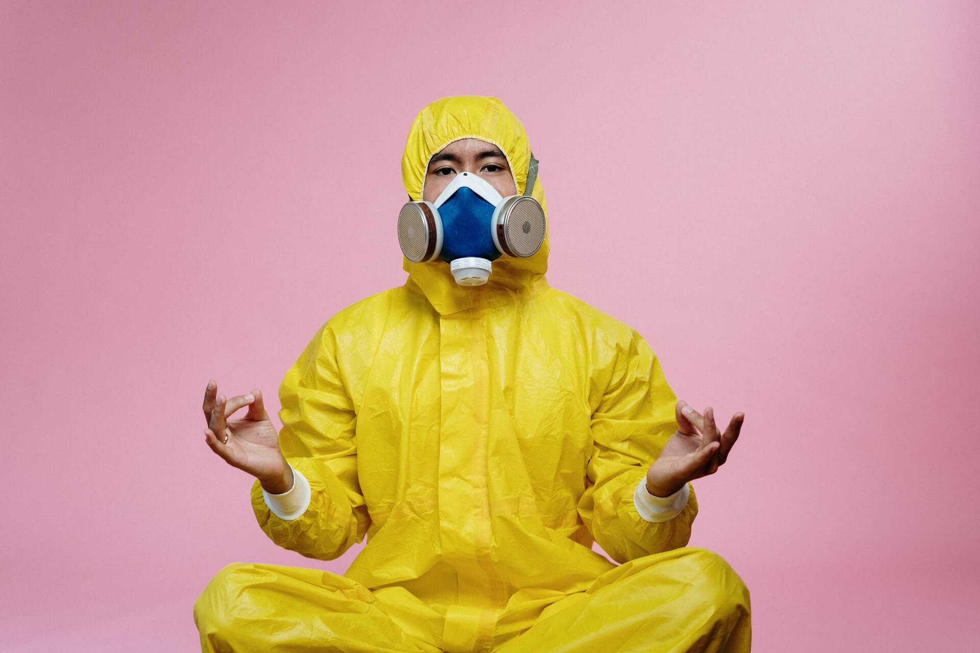 man sitting down with peace fingers in yellow hazmat suit and respirator